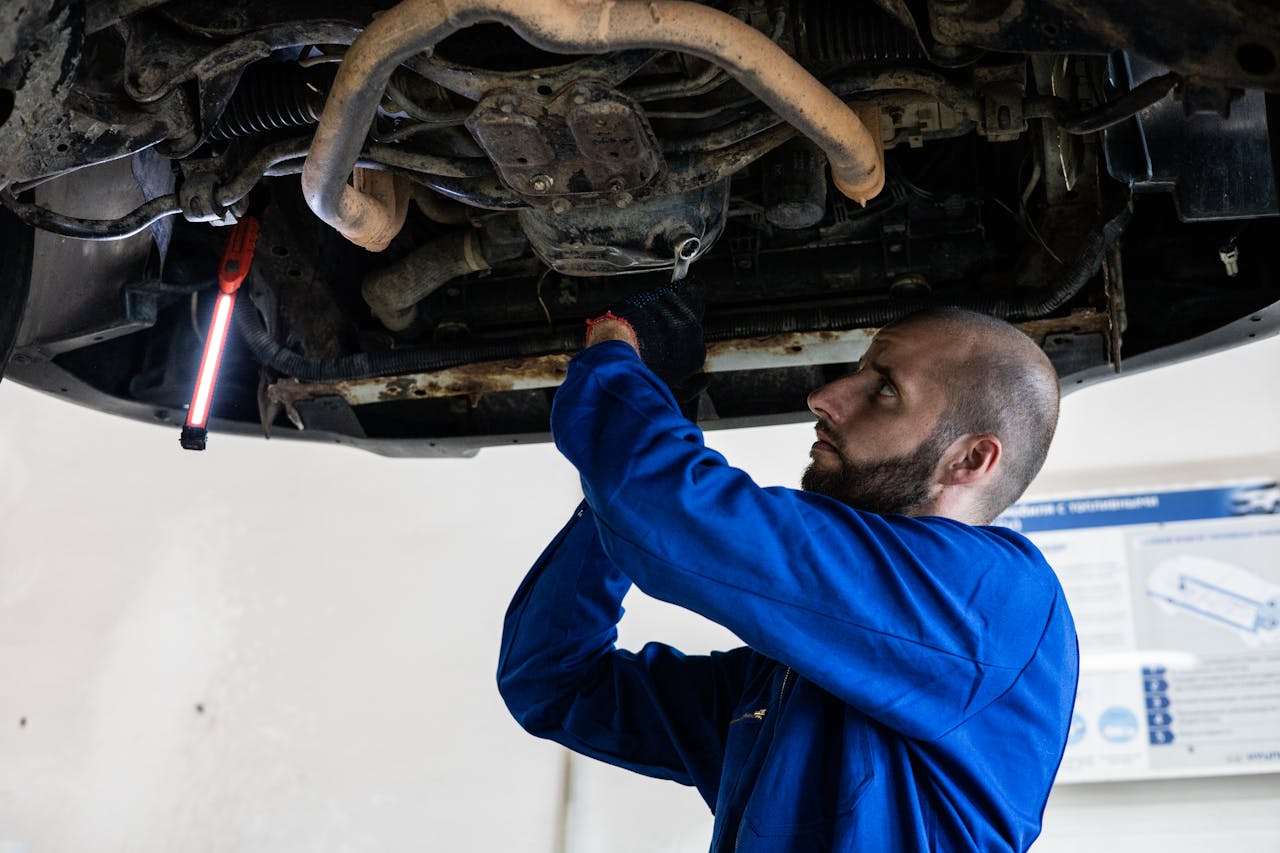 pexels-photo-8986101 Mechanic in blue coveralls works under a car, focusing on repairs in a garage setting.